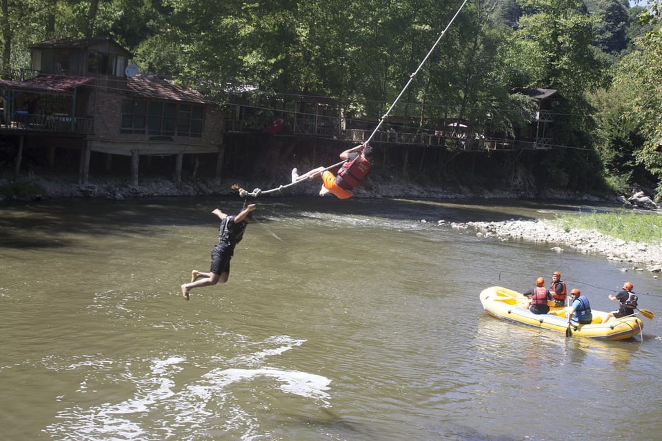 Melen Çayı üzerindeki halat kaydırağından suya doğru inen ziyaretçi ve altta bekleyen sarı rafting botu
