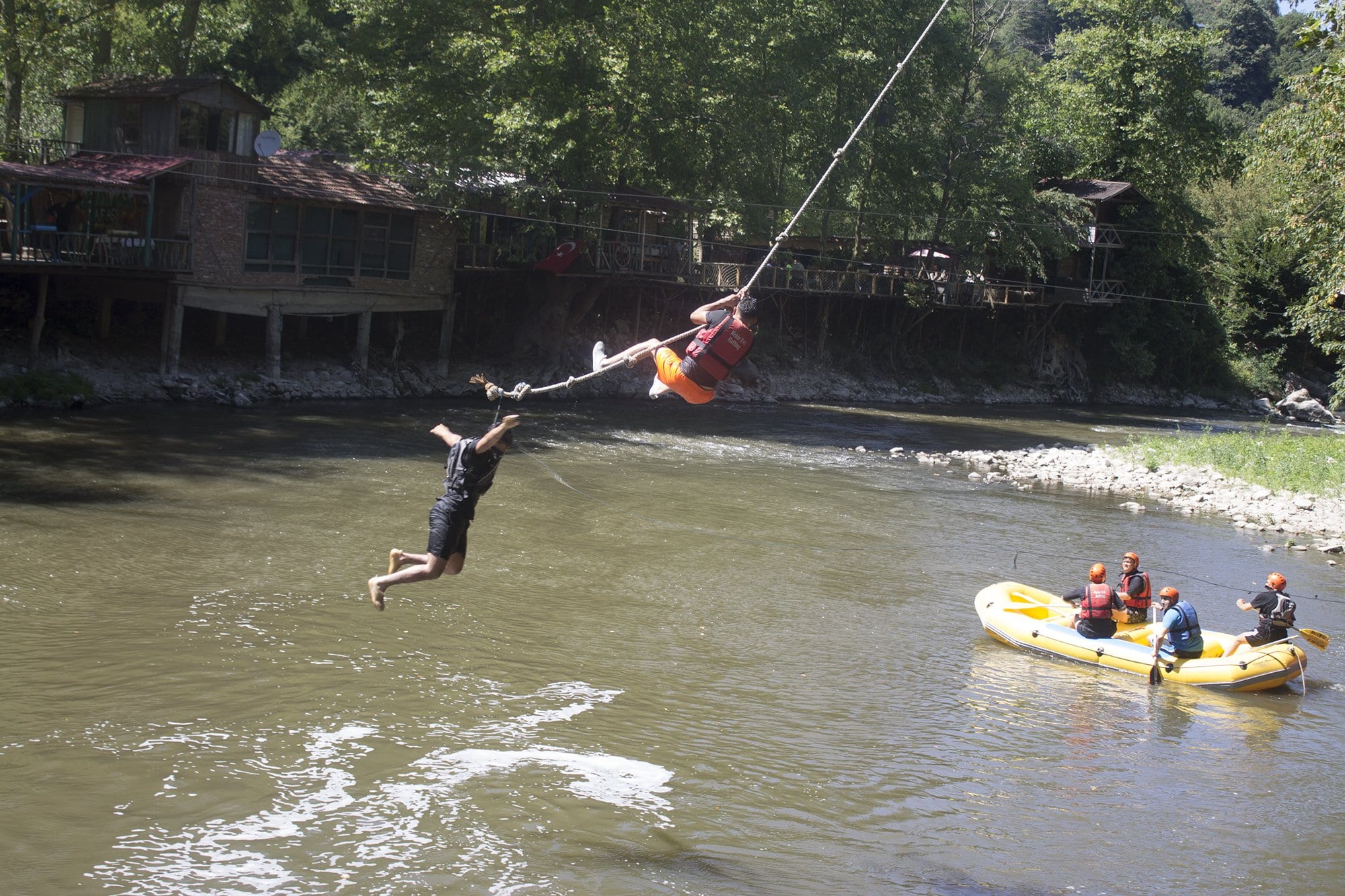Melen Çayı üzerindeki halat kaydırağından suya doğru inen ziyaretçi ve altta bekleyen sarı rafting botu
