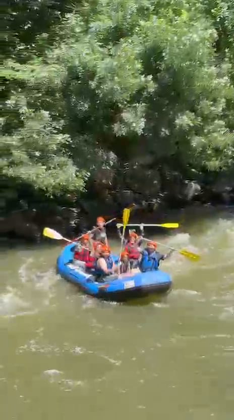Melen Çayı rafting parkurunda kayaların arasındaki köpüklü akıntıyı aşan mavi bot ve kürek çeken kasklı katılımcılar