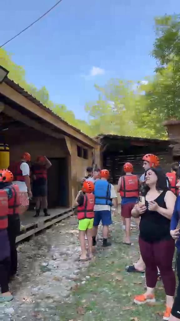 Rafting ekipmanı deposunda duvarda asılı can yeleklerinden seçim yapan ve kask takan katılımcı grubu
