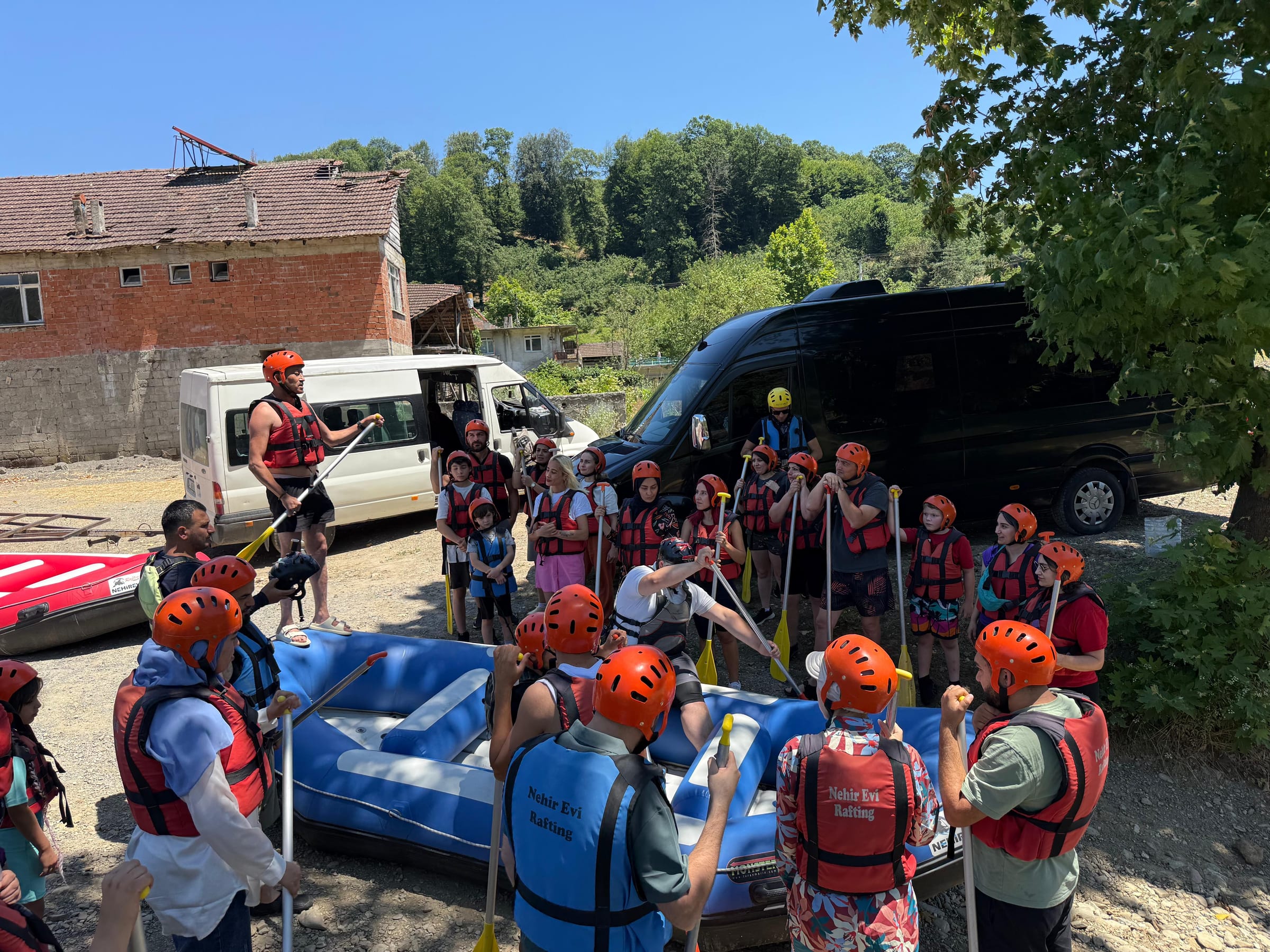 Düzce rafting organizasyonunda parkur öncesi kürekleriyle poz veren, kırmızı kask ve can yeleği takan kalabalık rafting grubu