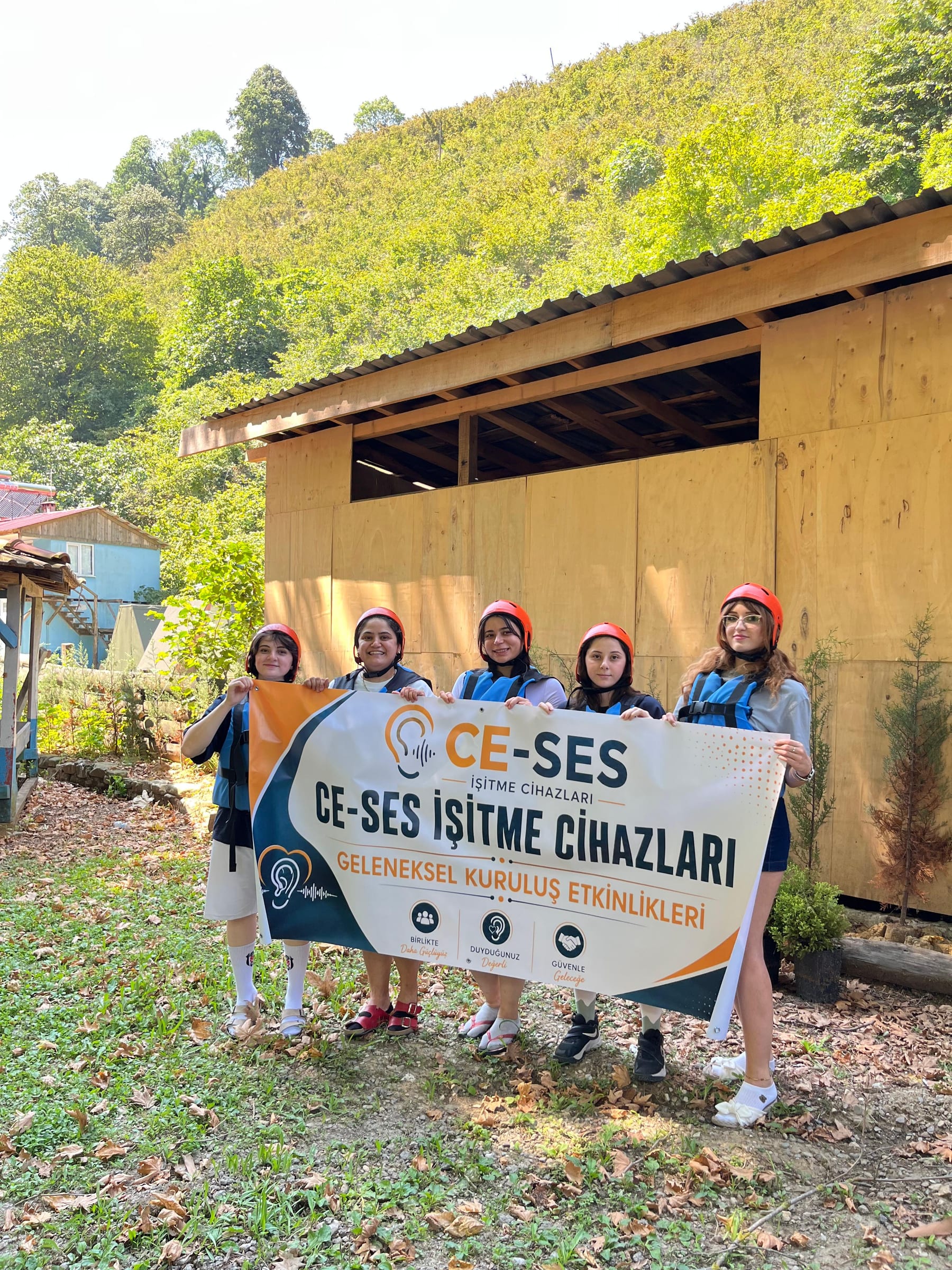 Melen Çayı rafting turuna katılan CE-SES ekibinin kuruluş etkinliği pankartıyla ahşap yapı önündeki toplu fotoğrafı