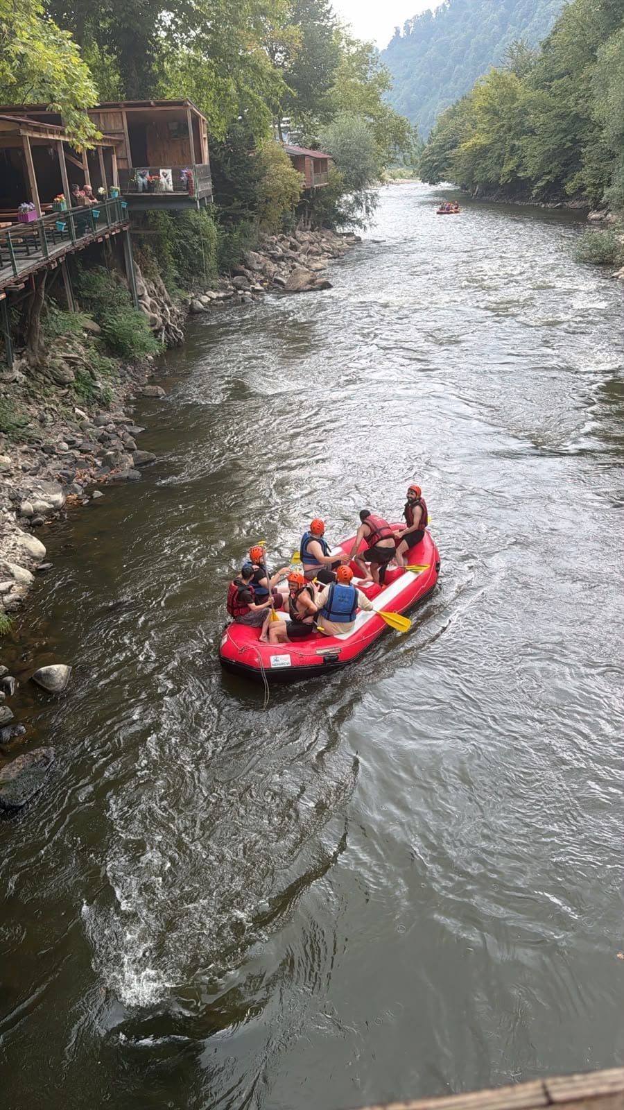 Melen Çayı rafting parkurunda köpüklü akıntıdan geçen kırmızı bot ve turuncu kask takan katılımcılar