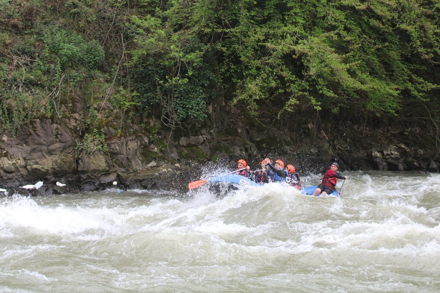 Düzce rafting parkurunda dar kaya boğazından geçen bot ve botun hemen yanında suda süzülen kırmızı yelekli katılımcı