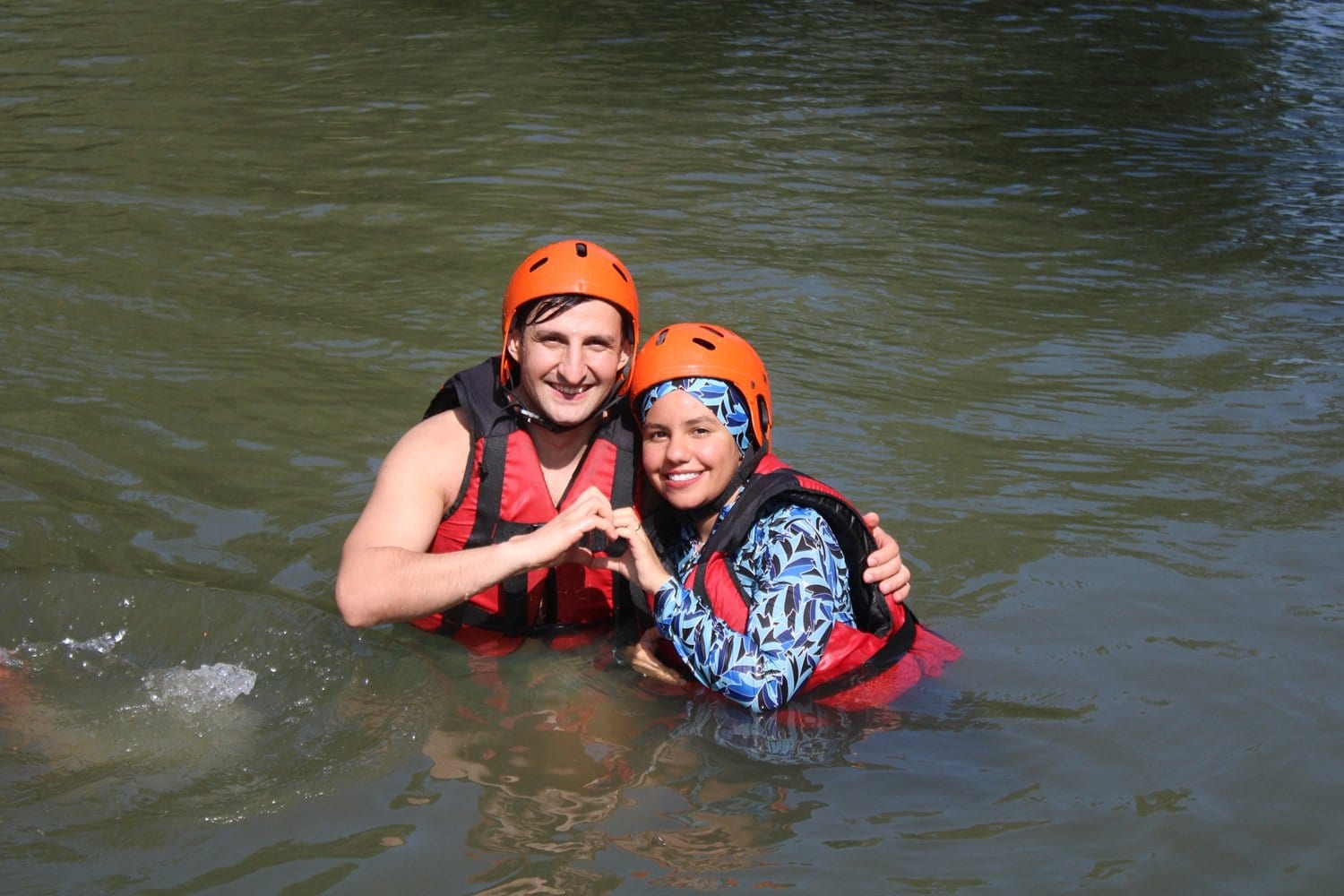 Melen Çayı suyunda kask ve can yeleğiyle elleriyle kalp işareti yapan iki rafting katılımcısı